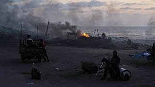 People sit near makeshift burners along the Sea Road in the south of Gaza City, 21 August, 2025