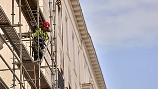 A construction worker stand on a scaffold in Madrid, Spain, Tuesday, Aug. 12, 2025