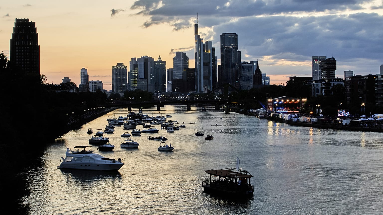 Boote liegen im Wasser auf dem Main, während ein Orchester während eines klassischen Open-Air-Konzerts in Frankfurt, Deutschland, auftritt. 21. August 2025.
