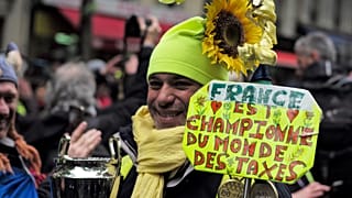 Un manifestante de los chalecos amarillos sostiene un cartel en el que se lee 'Francia es la campeona mundial de los impuestos' durante una protesta en París en 2019,