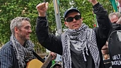 Liam O'Hanna, azaz Mo Chara, jobbról a második, a Kneecap együttes tagja, a bíróságról távozó támogatóihoz beszél, London, 2025. augusztus 20,
