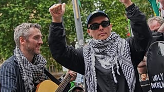 Liam O'Hanna, azaz Mo Chara, jobbról a második, a Kneecap együttes tagja, a bíróságról távozó támogatóihoz beszél, London, 2025. augusztus 20,