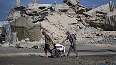 فلسطينيون يدفعون كرسيا متحركا يحمل أكياس طحين تم تفريغها من قافلة مساعدات إنسانية على مشارف بيت لاهيا, شمال قطاع غزة, يوم السبت, أغسطس. 23, 2025. (