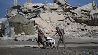 فلسطينيون يدفعون كرسيا متحركا يحمل أكياس طحين تم تفريغها من قافلة مساعدات إنسانية على مشارف بيت لاهيا, شمال قطاع غزة, يوم السبت, أغسطس. 23, 2025. (