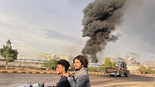 People ride a motorbike as smoke billows following Israeli airstrikes on multiple areas including a power planet and a gas station in Sanaa, Yemen, Sunday, Aug. 24, 2025.