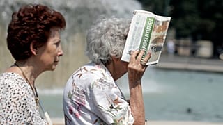 An elderly woman covers her face from the hot sun with a newspaper, in Milan, Italy, Thursday, 25 July 2019.
