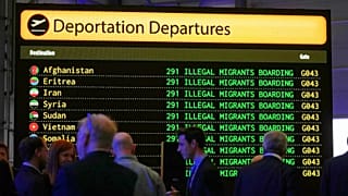 People stand in front of a mock departures board before Reform UK party leader Nigel Farage speaks a press conference at Oxford Airport, 26 August, 2025