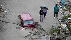 Menschen stehen neben einem festgefahrenen Auto nach den plötzlichen Überschwemmungen am Ufer des Tawi-Flusses in Jammu, Indien, am Mittwoch, den 27. August 2025.