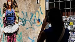 Una donna fotografa il quadro "Angel", dipinto dall'artista di strada Harry Grebe all'inizio dell'anno e dedicato ai giornalisti uccisi a Gaza, a Roma, lunedì 25 agosto 2025.