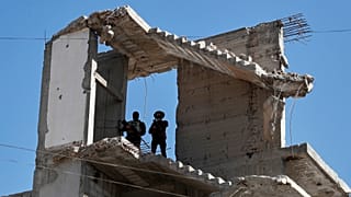 Agentes de segurança sírios montam guarda num edifício danificado pela guerra em Zamalka, nos arredores de Damasco, Síria, quinta-feira, 21 de agosto de 2025.