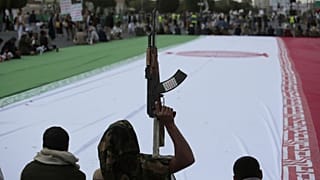 هواداران حوثی در جریان یک راهپیمایی هفتگی ضد آمریکایی و ضد اسرائیلی در صنعا، یمن، جمعه، ۲۰ ژوئن ۲۰۲۵ یک پرچم بزرگ از ایران را احاطه کرده‌اند.