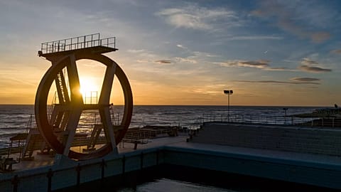The sun sets behind the diving boards of the swimming pool of a closed beach resort in Rome's Ostia beach, 21 November, 2024