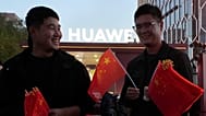 Hombres chinos reparten banderas nacionales durante las fiestas nacionales cerca de una tienda pop-up de Huawei en Pekín, el miércoles 2 de octubre de 2024.