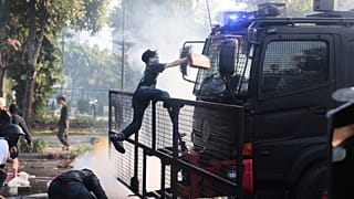 Un hombre sube a un camión de la policía con cañones de agua durante una protesta tras la muerte de un mensajero en los enfrentamientos entre la policía antidisturbios y los estudiantes.