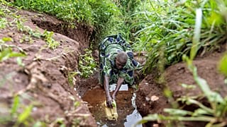 Joy Okwanjire, in ihren siebziger Jahren, füllt einen Krug als Teil ihrer täglichen Wanderung durch steile Hügel, um Wasser aus einem über einen Kilometer entfernten Bach zu holen, am 20. Oktober 2024 in Mubushuro, Uganda.