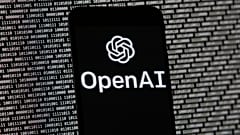 The OpenAI logo appears on a mobile phone in front of a computer screen with random binary data, March 9, 2023, in Boston. 
