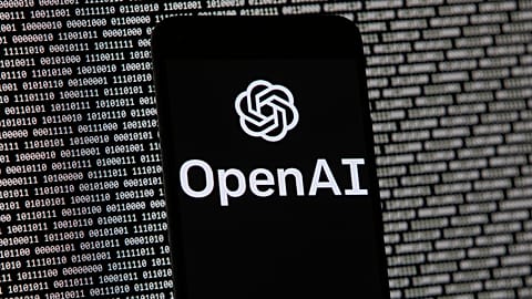 The OpenAI logo appears on a mobile phone in front of a computer screen with random binary data, March 9, 2023, in Boston. 