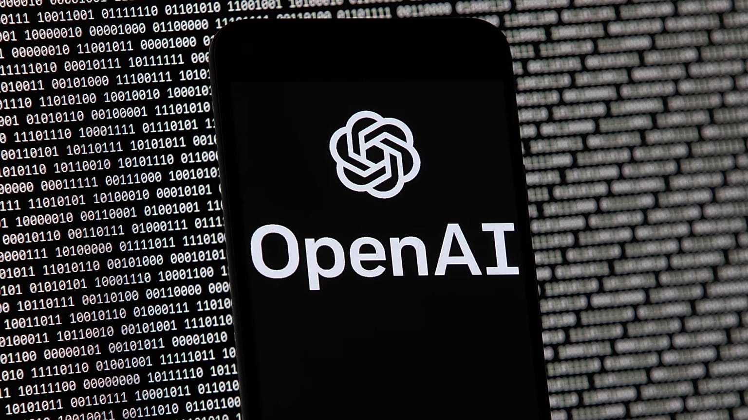 OpenAI logosu, Boston'da rastgele ikili veriler içeren bir bilgisayar ekranının önündeki bir cep telefonunda görünüyor, 9 Mart 2023.