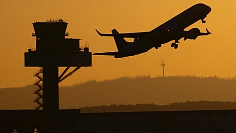 Utasszállító repülőgép száll fel a frankfurti repülőtérről a nap utolsó fényében, a német légiforgalmi irányítás (DFS) tornya mellett elrepülve, Frankfurt/Mainban, Németországban.