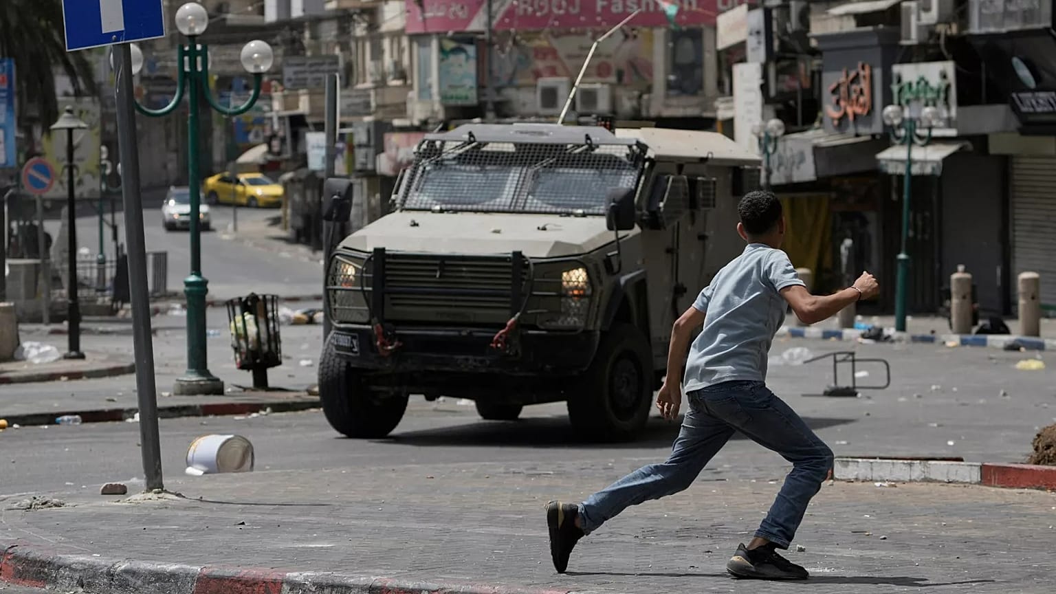 Un palestinese corre davanti a un veicolo blindato durante scontri con le forze israeliane dopo un raid militare nella città di Nablus, in Cisgiordania, il 27 agosto 2025
