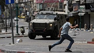 Un Palestinien court devant un véhicule blindé lors d'affrontements avec les forces israéliennes après un raid militaire dans la ville de Naplouse en Cisjordanie, le 27 août 2025