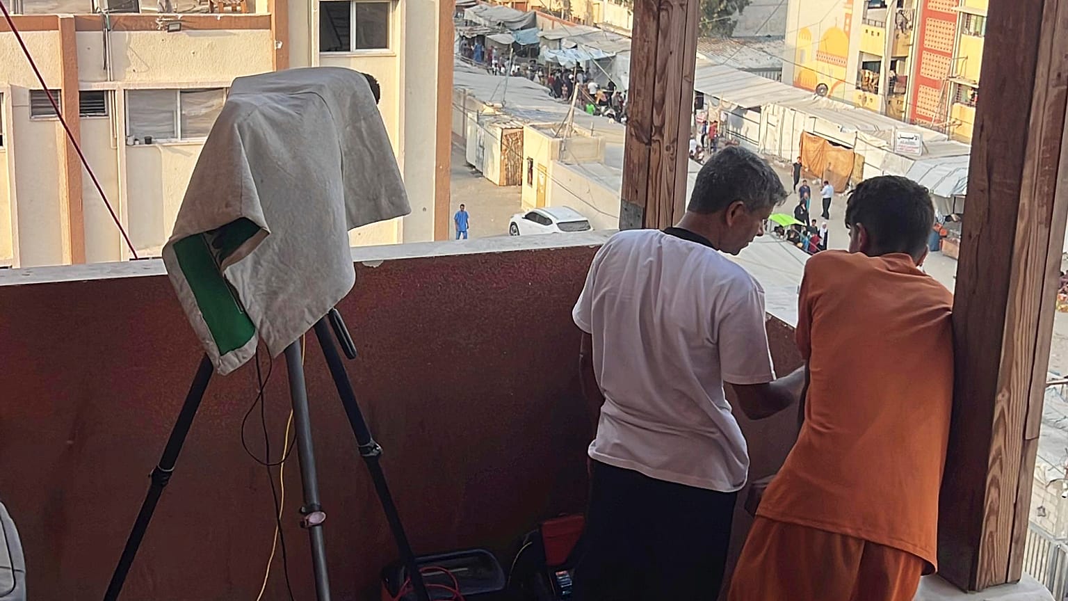 تظهر هذه الصورة، الملتقطة في 13 أغسطس/ آب 2025، مصور رويترز حسام المصري، مرتديًا قميصًا أبيض، واقفا بجوار كاميرا الفيديو الخاصة به المغطاة بمنشفة على درج مستشفى ناصر.