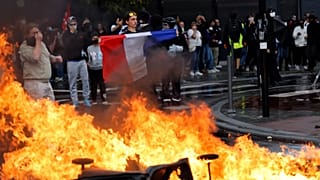 A protester of the "Block Everything" movement displays a French national flag next to burning rubbish bins in Lille, 10 September, 2025