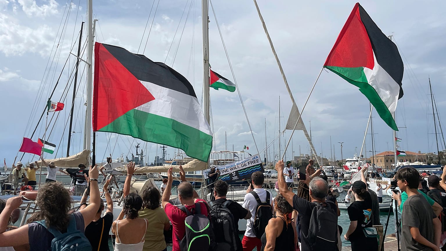 People carry Palestinian flags as they bid farewell to the Italian fleet of the Global Sumud Flotilla departing from the port of Siracusa, Italy