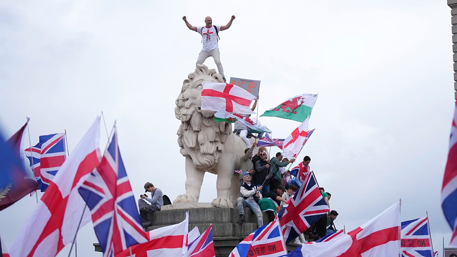 A demonstrator stands on the head of one of the lions of Westminster Bridge during a Tommy Robinson-led Unite the Kingdom march and rally in London, Saturday Sept. 13, 2025.