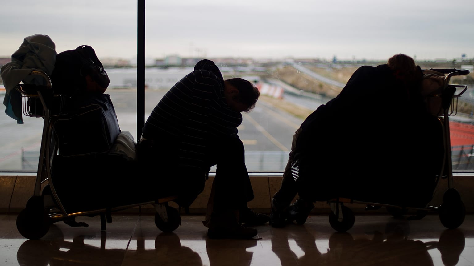 Dos pasajeros duermen en carritos de equipaje en el Aeropuerto de Barajas, Madrid, el domingo 5 de diciembre de 2010.