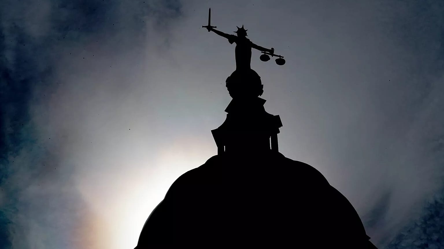 A statue of liberty is silhouetted as it stands atop the Old Bailey in London, 8 August, 2019