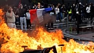 A protester of the "Block Everything" movement displays a French national flag next to burning cabbage bins in Lille, northern France, Wednesday, Sept. 10, 2025. 