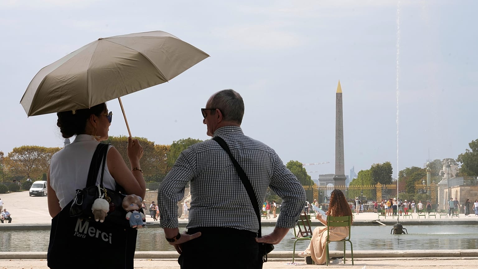 Des personnes sous un parapluie regardent une fontaine dans le jardin des Tuileries, le mercredi 13 août 2025 à Paris, en France