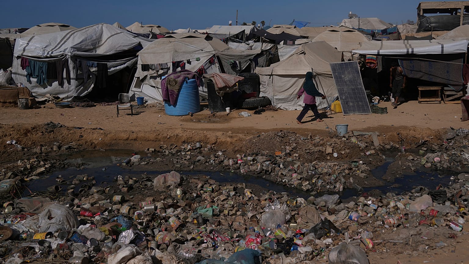 Une Palestinienne passe devant des eaux usées à ciel ouvert dans une zone d'un camp de tentes de fortune pour personnes déplacées à Zawaida, dans le centre de la bande de Gaza