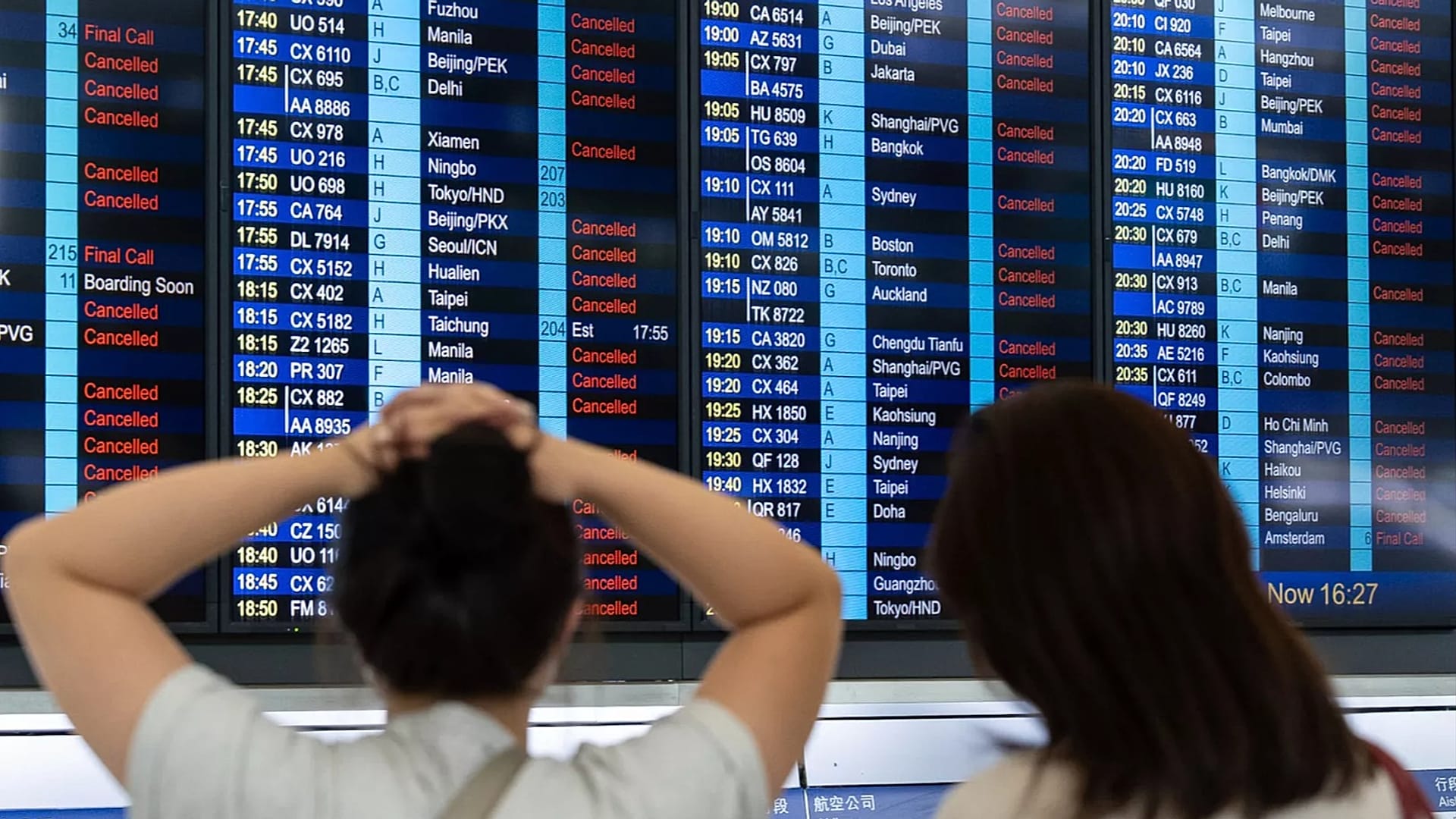 Passageiros olham para um painel informativo que mostra os voos cancelados devido ao super tufão Ragasa, no Aeroporto Internacional de Hong Kong.
