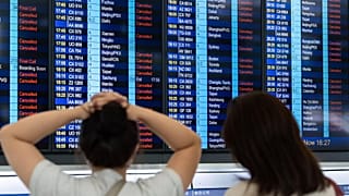 Passagiere schauen auf eine Informationstafel am internationalen Flughafen von Hongkong, auf der die wegen des Super-Taifuns Ragasa gestrichenen Flüge angezeigt werden.