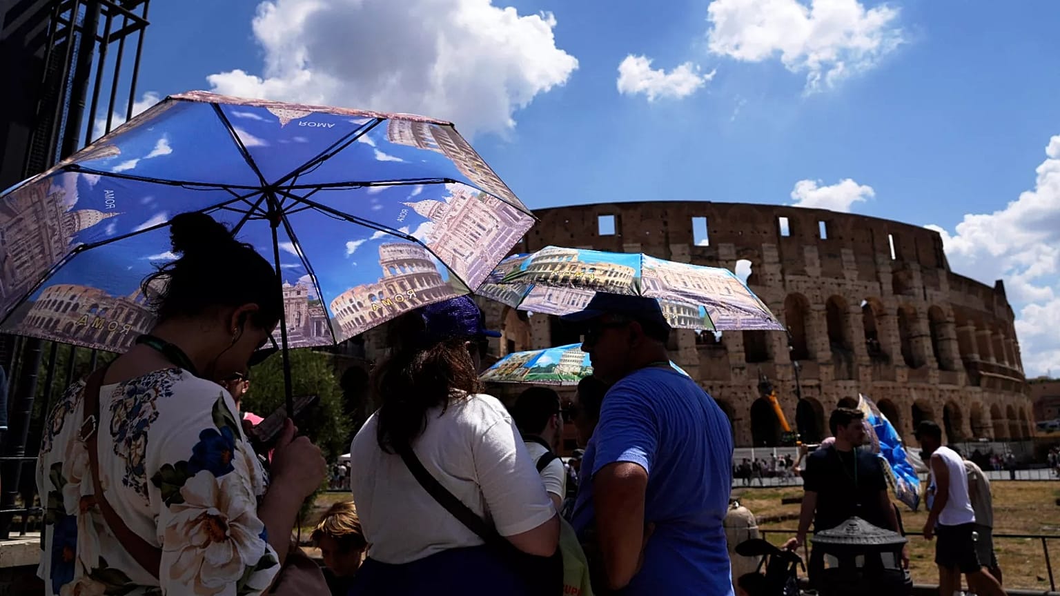 Tourists use umbrellas to shelter from the heat as they line up for a tour of the Forum in Rome in July 2025. 