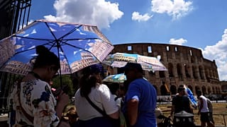 Tourists use umbrellas to shelter from the heat as they line up for a tour of the Forum in Rome in July 2025. 