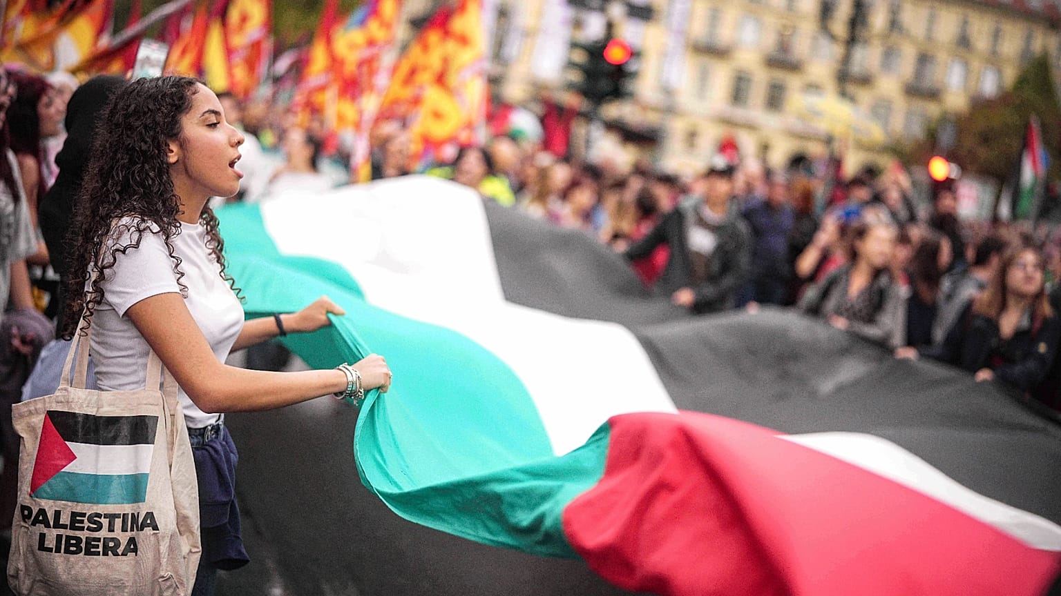 Manifestanti intonano slogan mentre tengono in mano un gigantesco faldone palestinese durante uno sciopero nazionale per protestare contro la guerra a Gaza, a Roma
