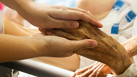 A health professional holds a patient's hand.