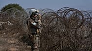A French UNIFIL peacekeeper looks through binoculars while standing on a hill overlooking Kfar Kila, 20 August, 2025