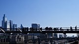People walk over Millenium Bridge with The City of London buildings in the background. 3 April 2025.