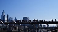 People walk over Millenium Bridge with The City of London buildings in the background. 3 April 2025.