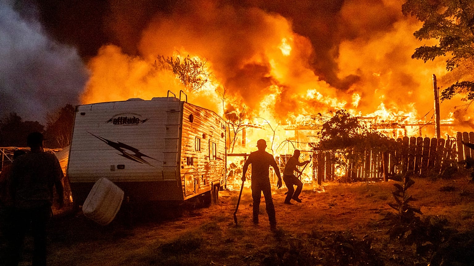 I residenti cercano di impedire che le fiamme di una casa in fiamme si propaghino a una casa vicina mentre l'incendio 6-5 attraversa la comunità di Chinese Camp, nella contea di Tuolumne, California