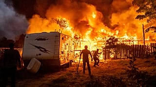 I residenti cercano di impedire che le fiamme di una casa in fiamme si propaghino a una casa vicina mentre l'incendio 6-5 attraversa la comunità di Chinese Camp, nella contea di Tuolumne, California