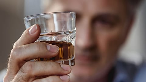 A man contemplates a glass of whisky.