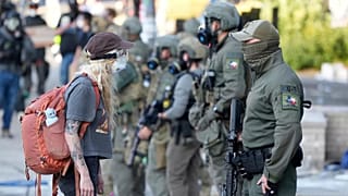 FILE - A woman stands off with a law enforcement officer wearing a Houston Field Office Special Response Team patch outside the U.S. Immigration and Customs (ICE) building dur