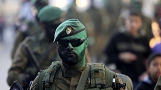 مسلحون من كتائب عز الدين القسام، الجناح العسكري لحركة حماس، يلوّنون وجوههم باللون الأخضر أثناء سيرهم في شوارع مخيم النصيرات للاجئين بوسط قطاع غزة