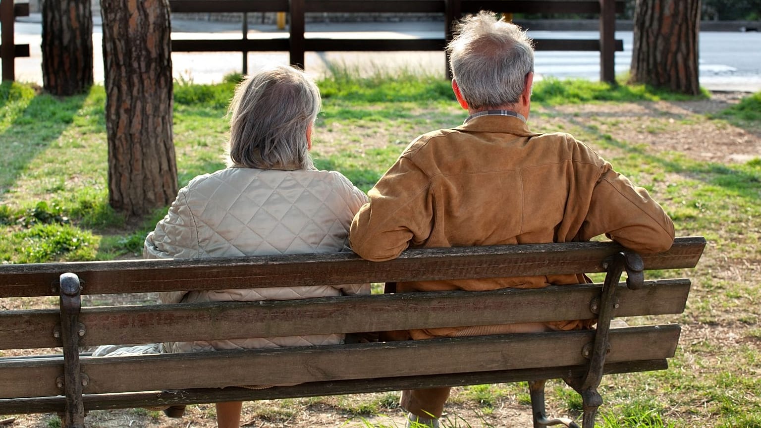 Uma mulher idosa e um homem sentam-se num banco de jardim.