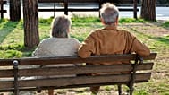 Uma mulher idosa e um homem sentam-se num banco de jardim.
